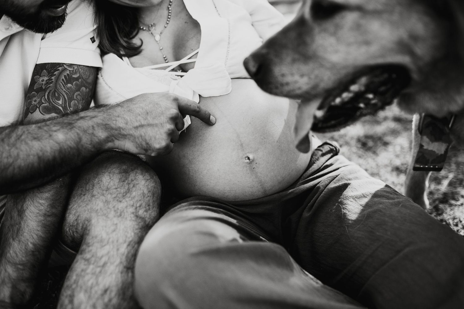 Black and white photo of a couple relaxing with their dog in a casual outdoor setting.
