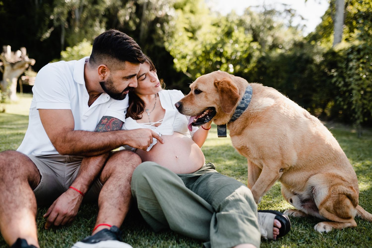 A couple and their dog share tender moments while relaxing on grass in a sunny garden.