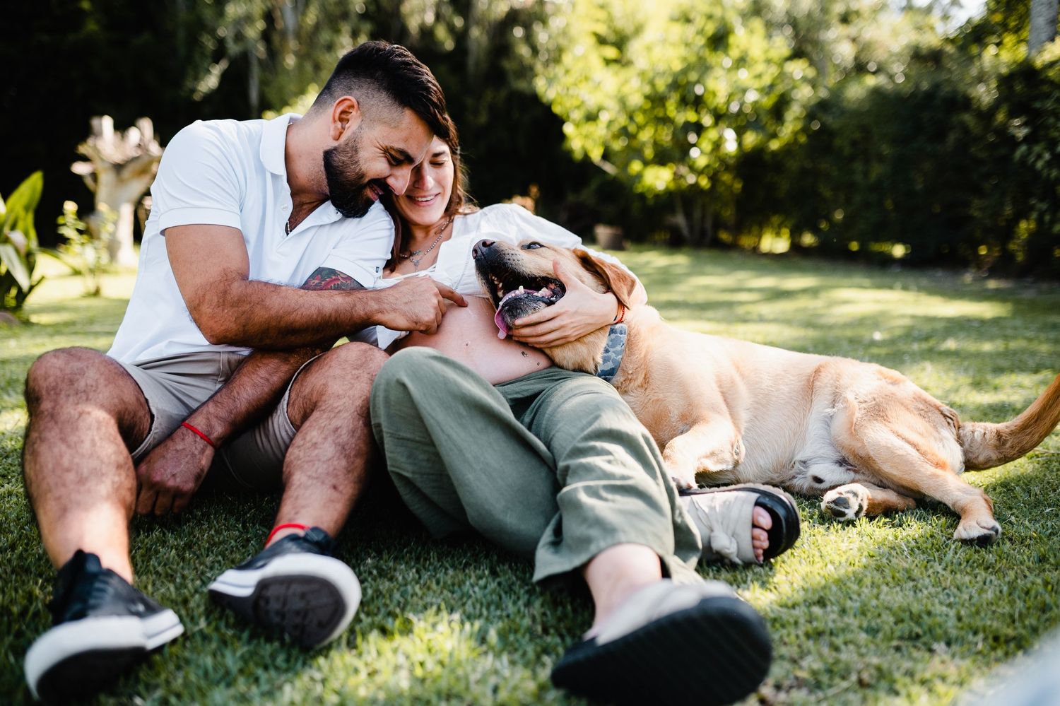 A couple shares an intimate moment while relaxing on grass in a sunny park setting.
