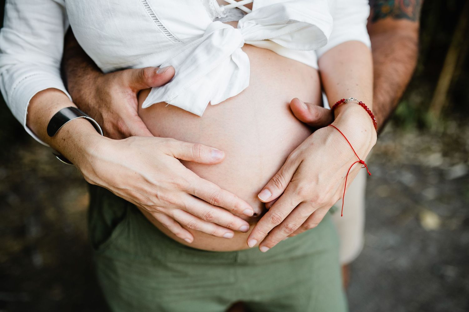 Close-up of hands tenderly cradling a pregnant belly against neutral background.