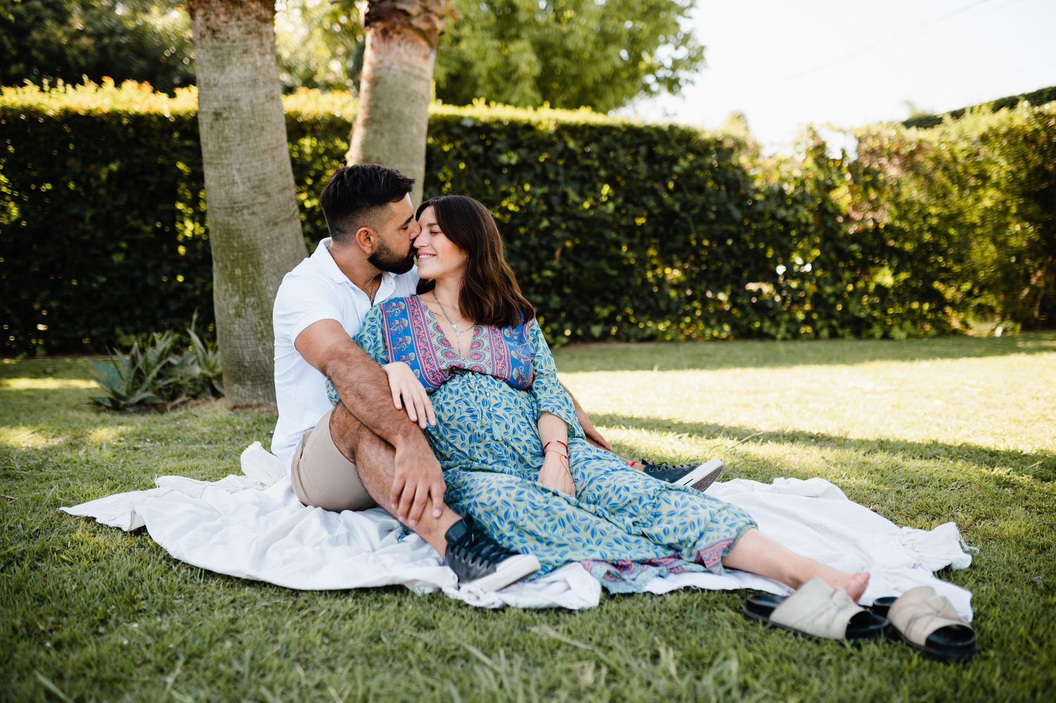 Couple relaxing together on a white blanket in a garden with palm trees during a sunny afternoon.