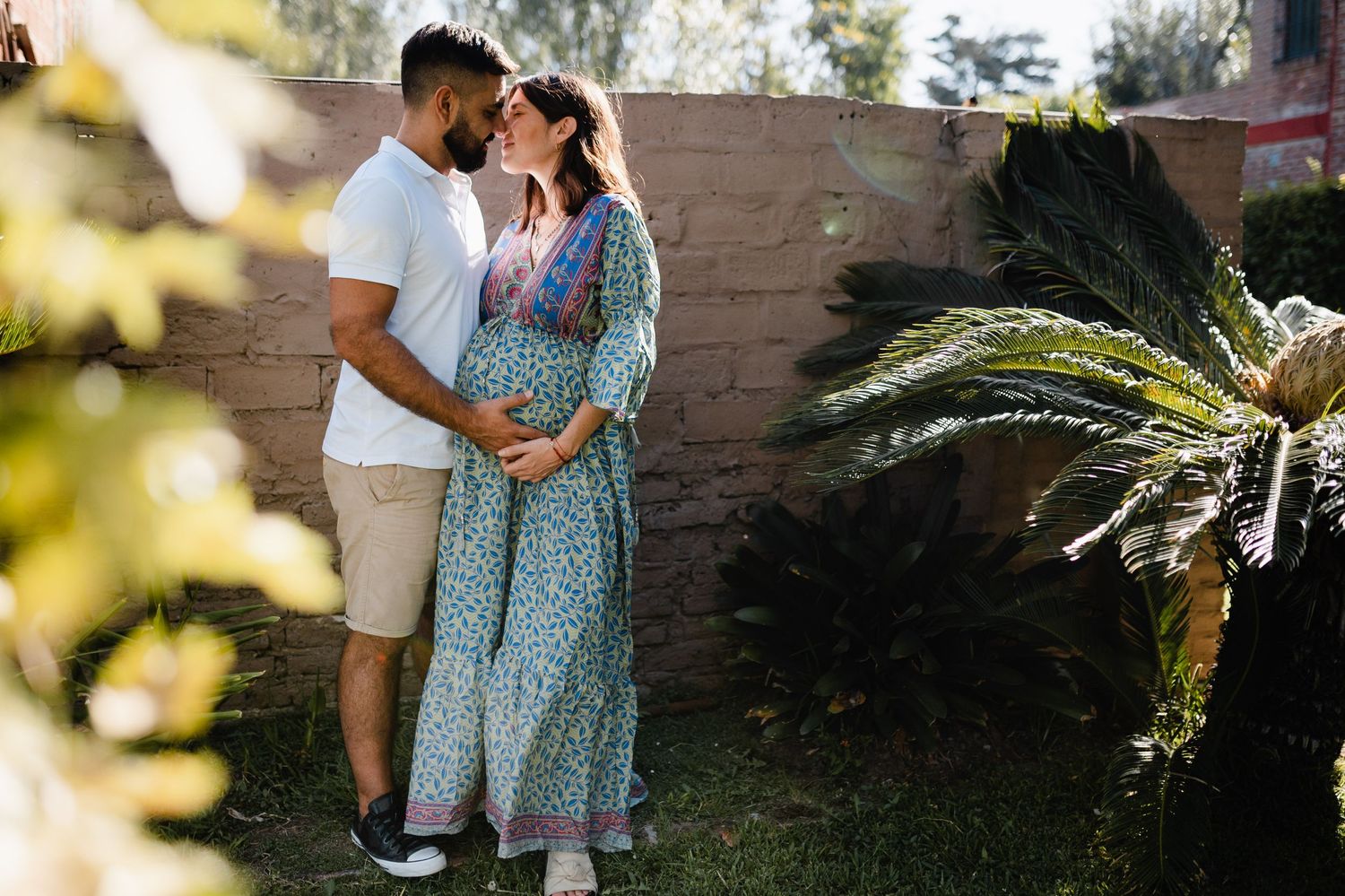 Couple standing together in garden setting during golden hour with palm plants in background.