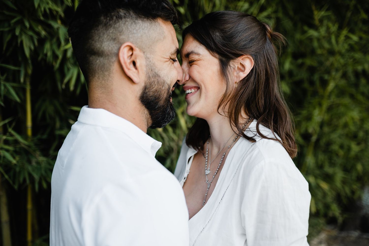An affectionate couple in white outfits embracing against a natural bamboo backdrop.