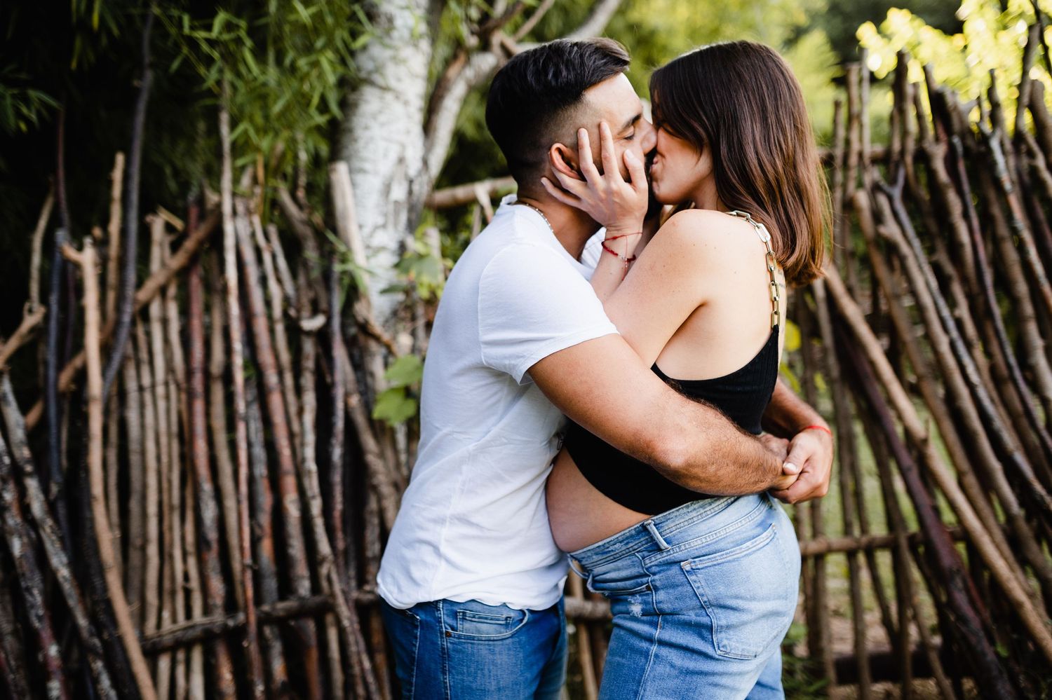 Intimate moment captured against rustic bamboo fence during maternity session.
