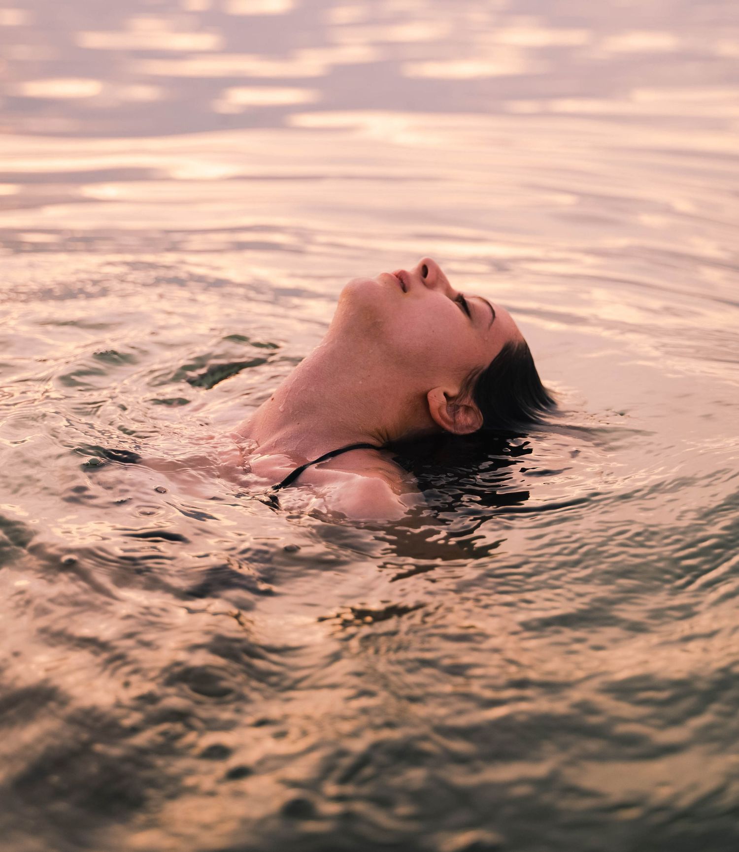 Someone floating in pink-tinted water at sunset with their head tilted back.