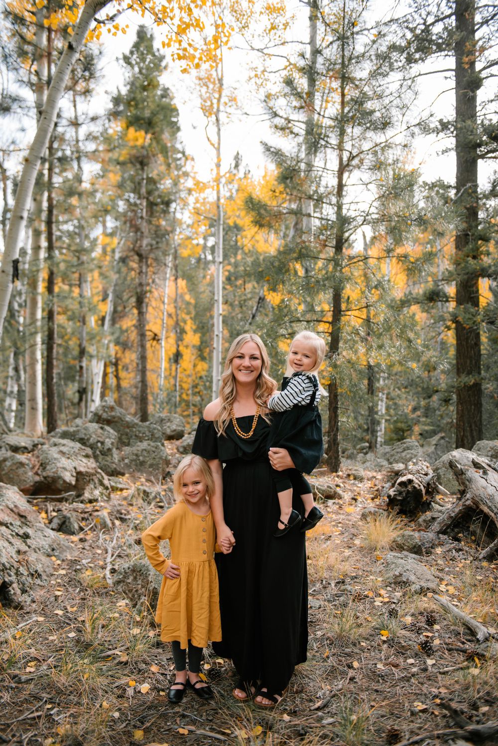Family portrait in an autumn aspen forest with golden leaves and rocky ground.