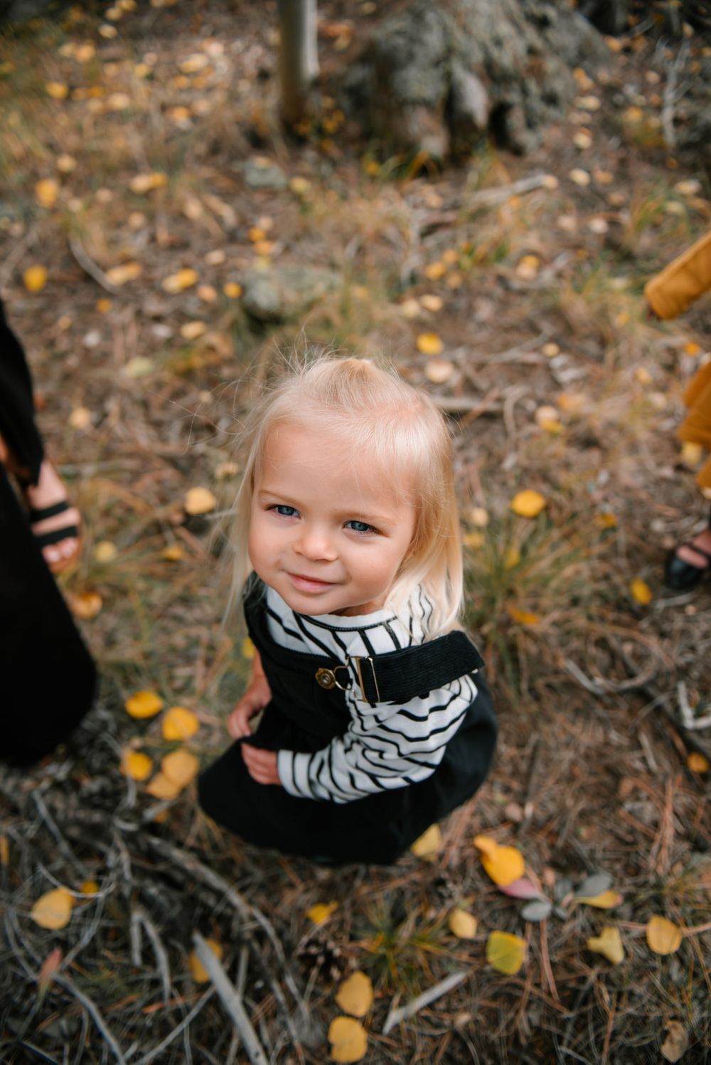 Child in black and striped outfit smiling in autumn forest setting.