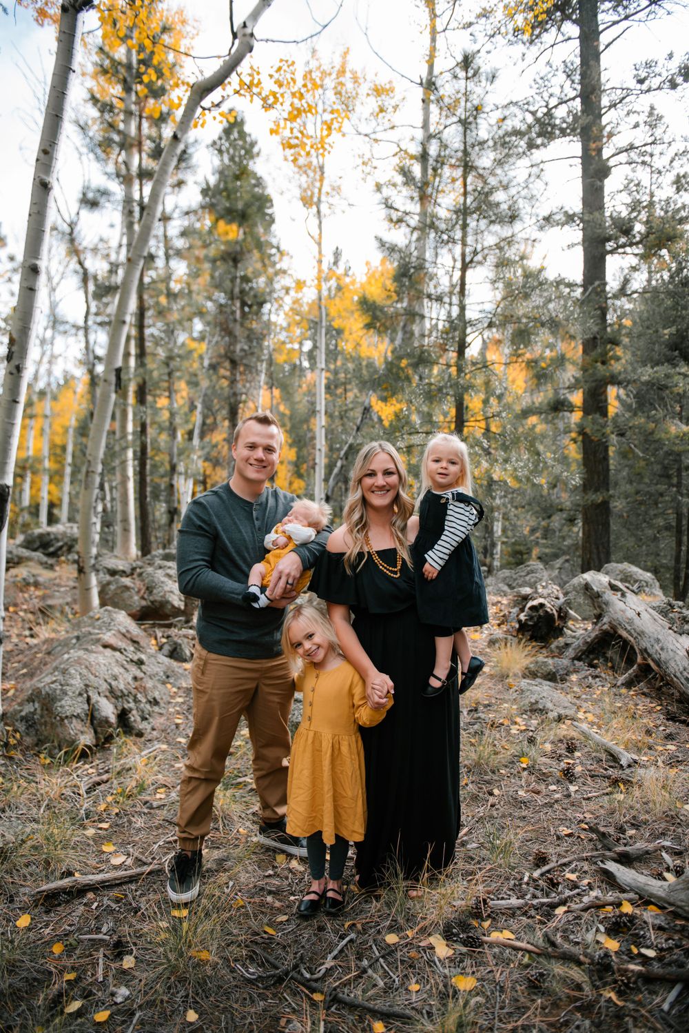 Family enjoying a playful moment together in an autumn forest with golden aspen trees and rocky terrain.