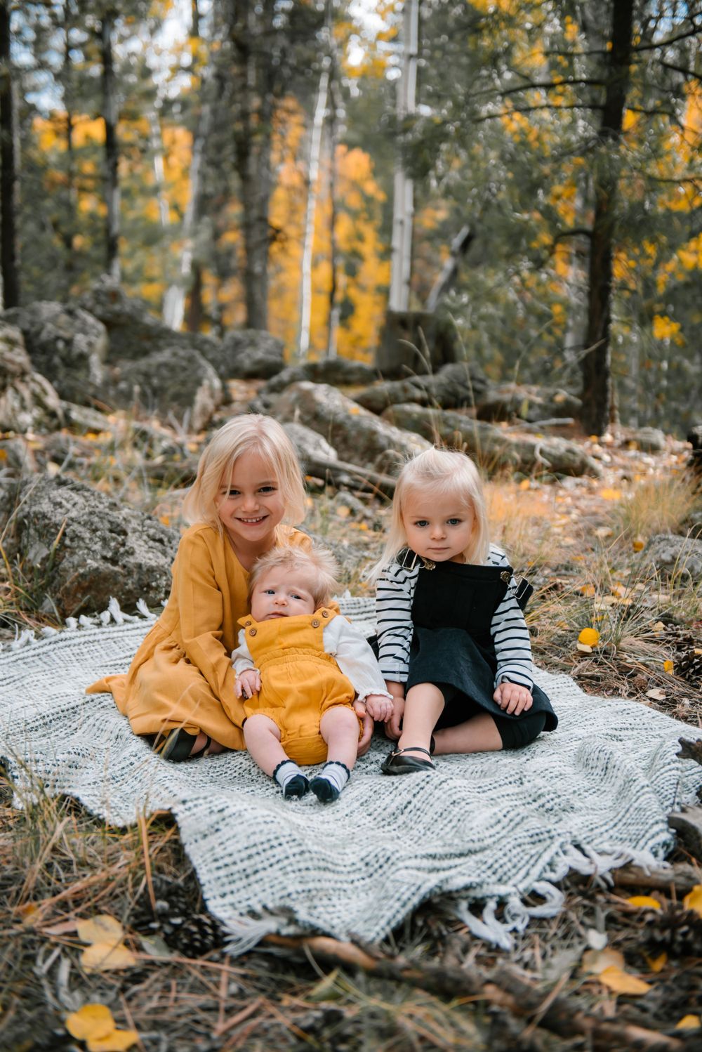 Children relaxing on a cozy blanket in a wooded area with golden autumn leaves.
