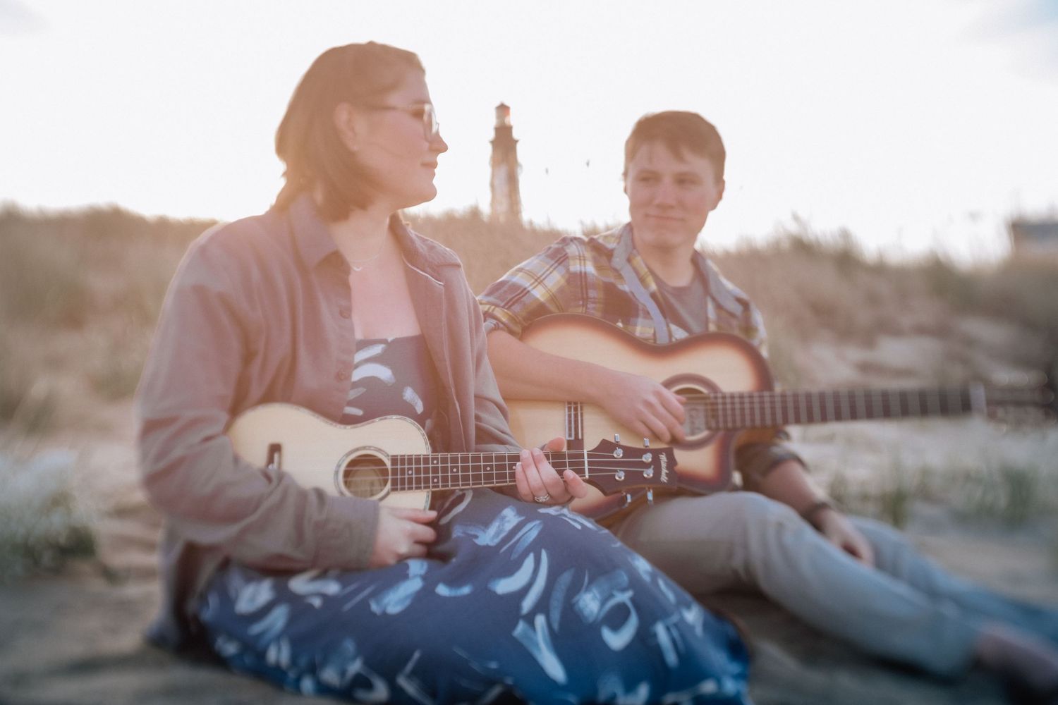 man and woman on the beach with a guitar and ukelele with lighthouse in the background in virginia beach