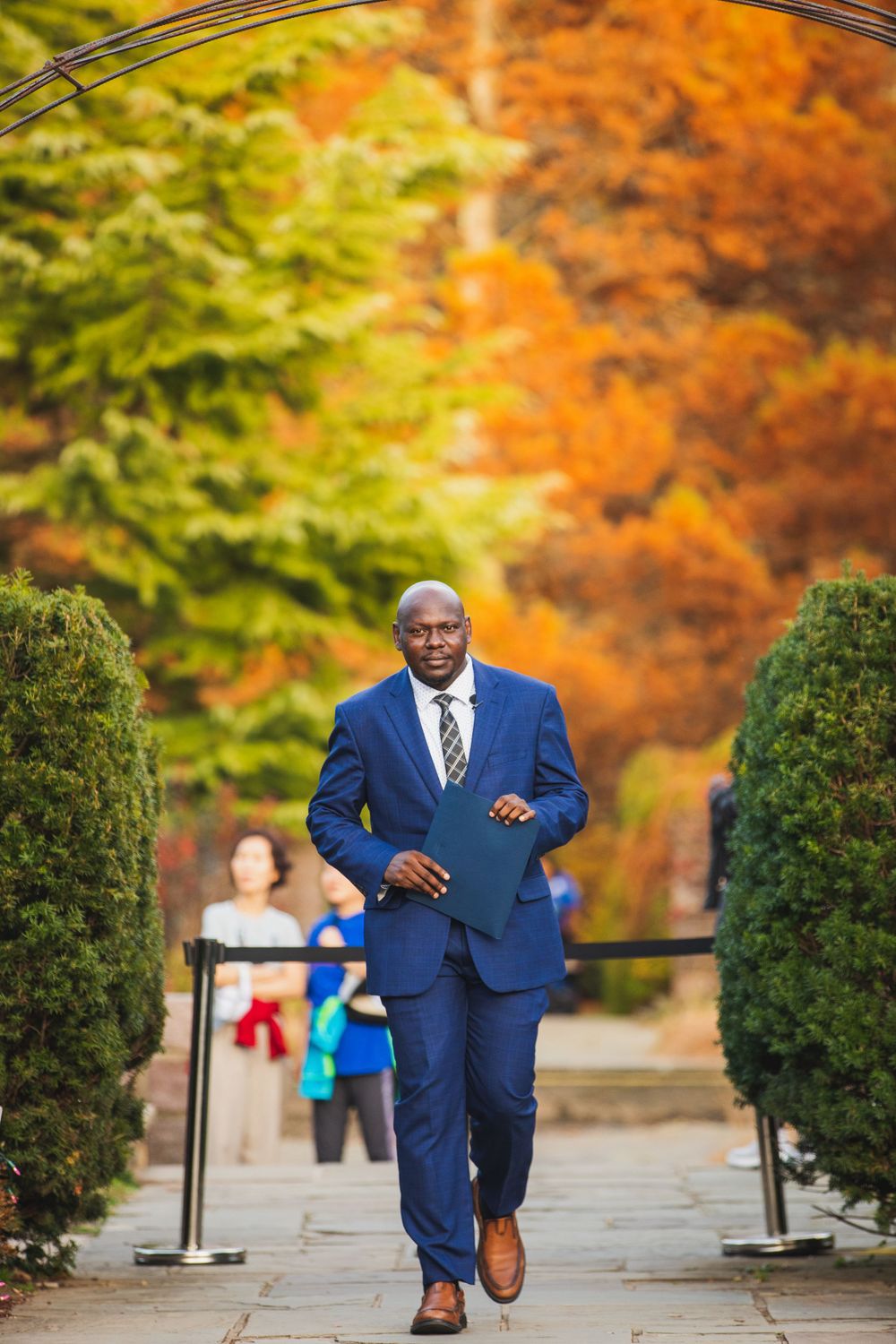 Person in bright blue suit walks down garden path with autumn foliage in background.