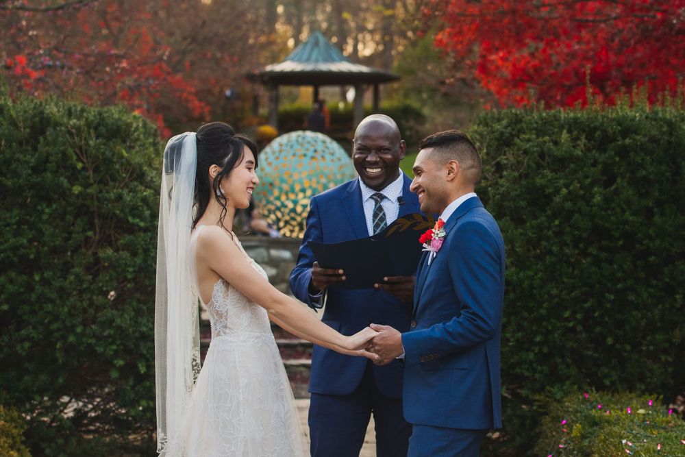 Intimate outdoor wedding ceremony with couple holding hands during vow exchange.