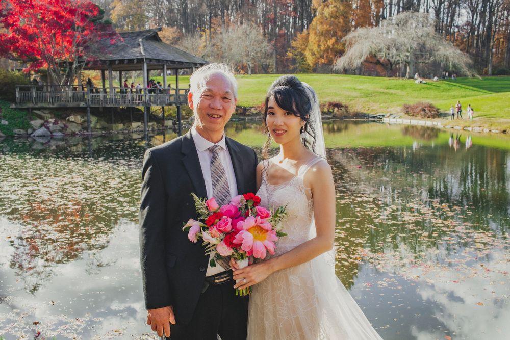 Bridal portrait by serene pond with bright red maple trees in background.