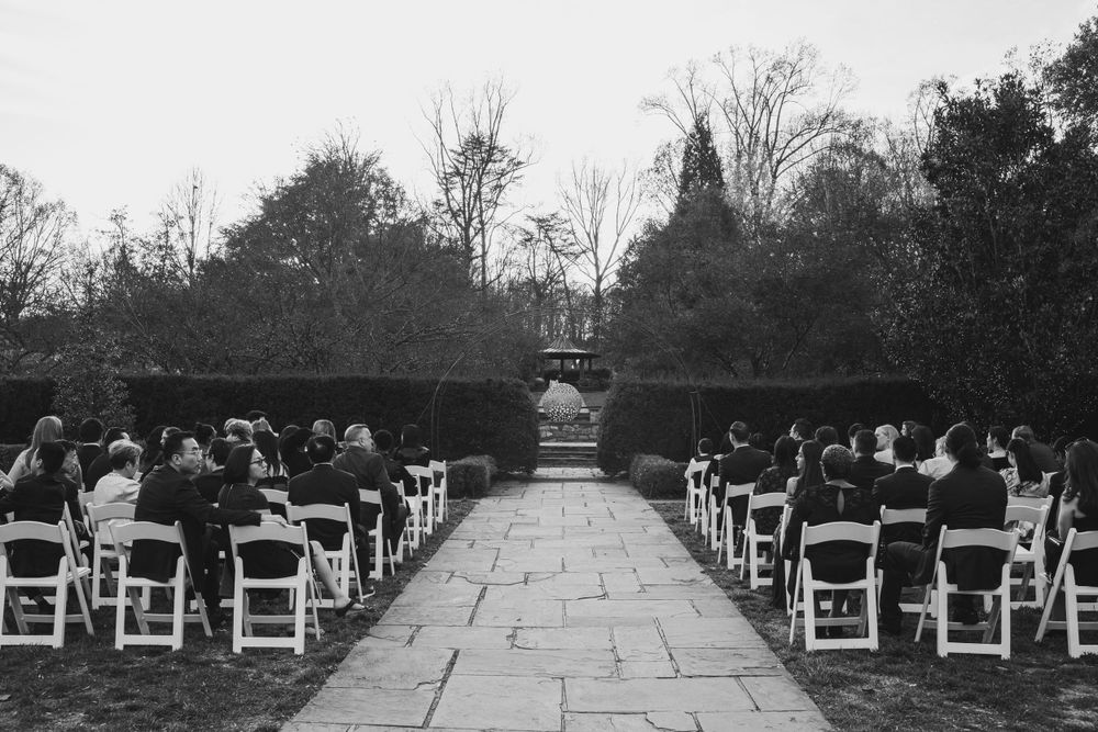 Black and white photo of empty chairs lined up along stone pathway at outdoor wedding venue.