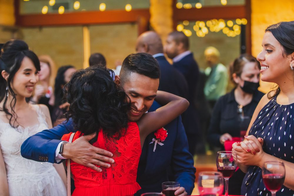 Wedding reception celebration with guests hugging and dancing in warm lit venue.