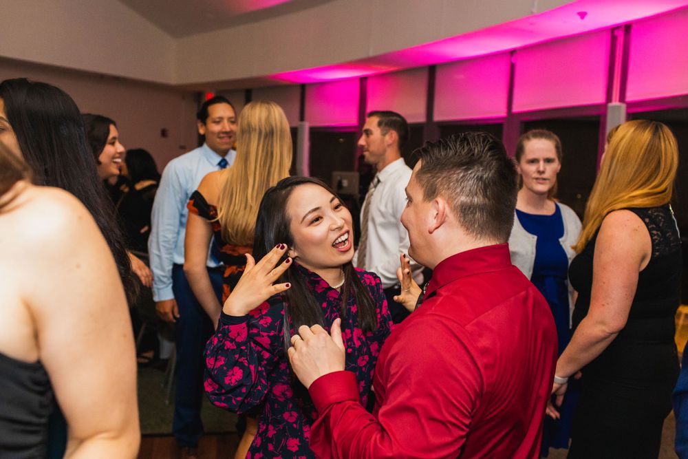 Party guests dancing and celebrating at an indoor event with pink ambient lighting.