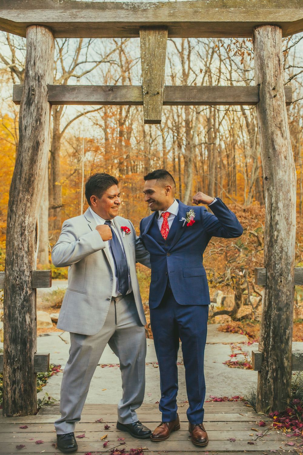 Groomsmen strike playful poses under wooden arch during autumn wedding photoshoot.