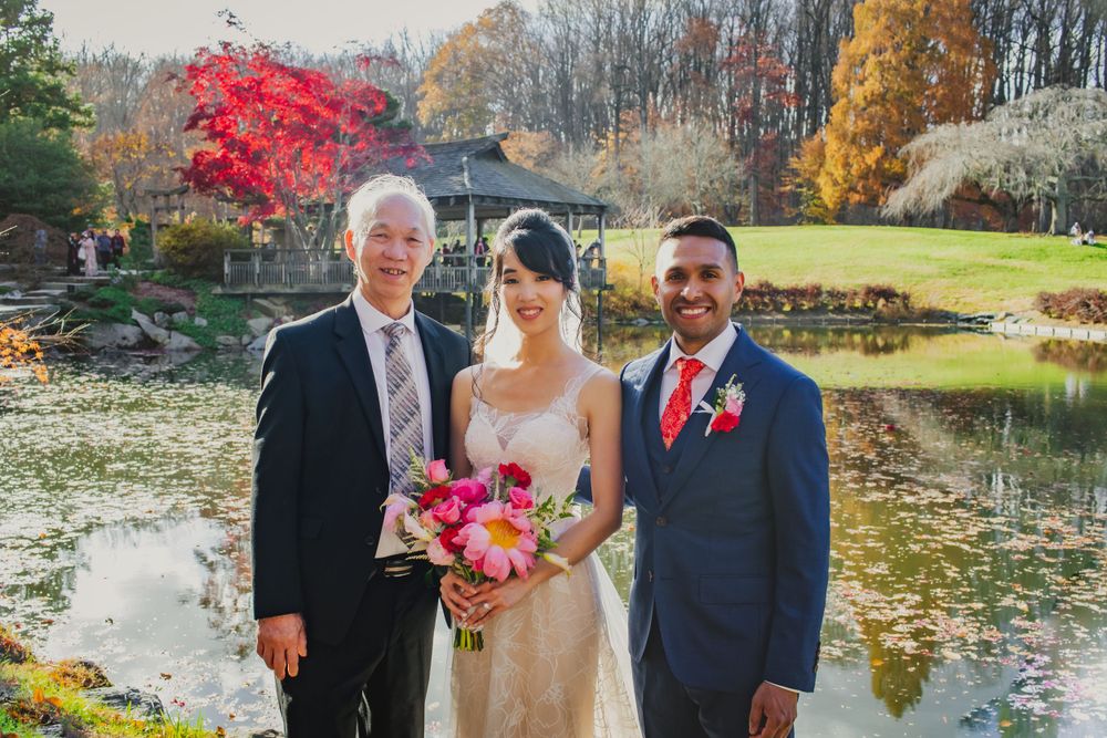 Wedding party poses by scenic pond with fall foliage and red maple trees.