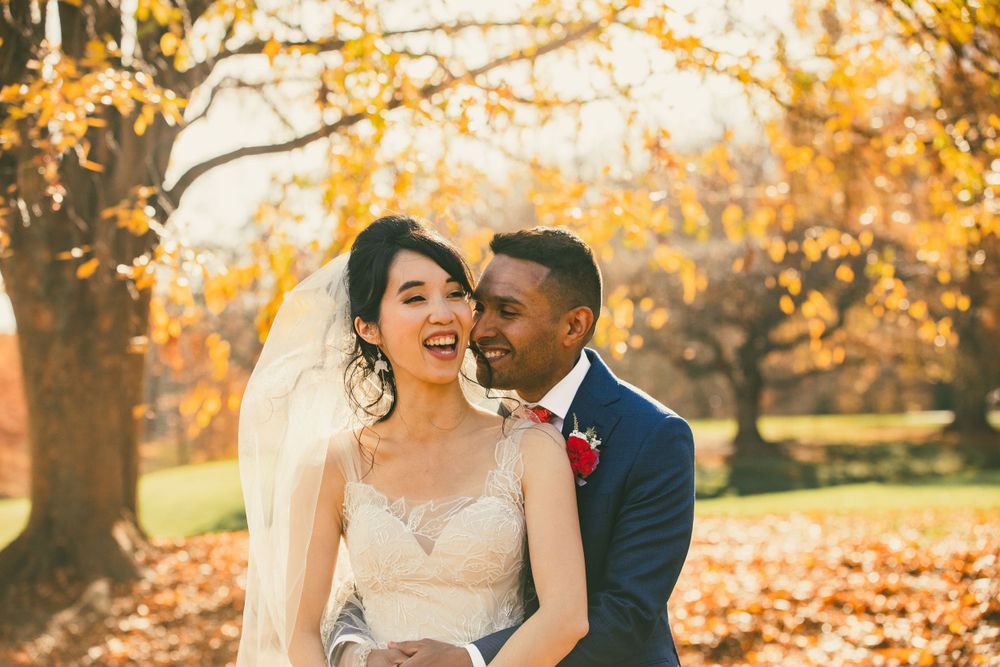 Groom hugs bride from behind with fall foliage backdrop at Brookside Garden before wedding.