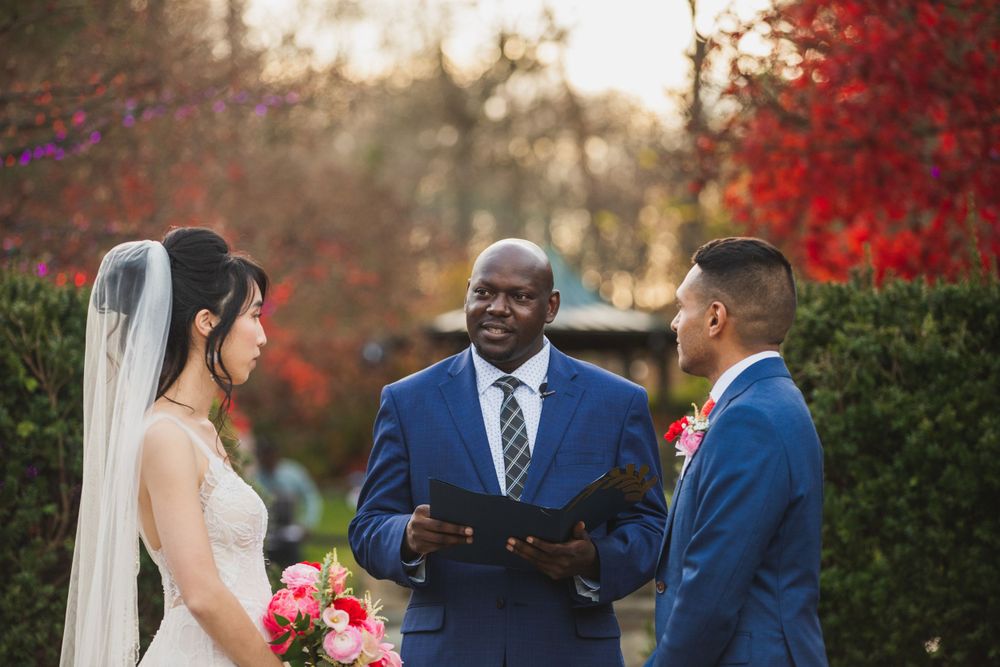 Outdoor wedding ceremony with officiant and couple exchanging vows amid fall foliage.