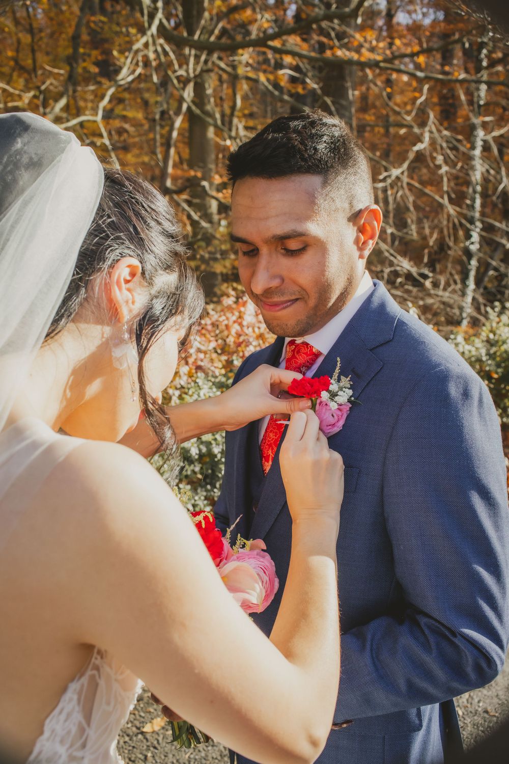 Intimate moment of boutonniere pinning during outdoor fall wedding ceremony.