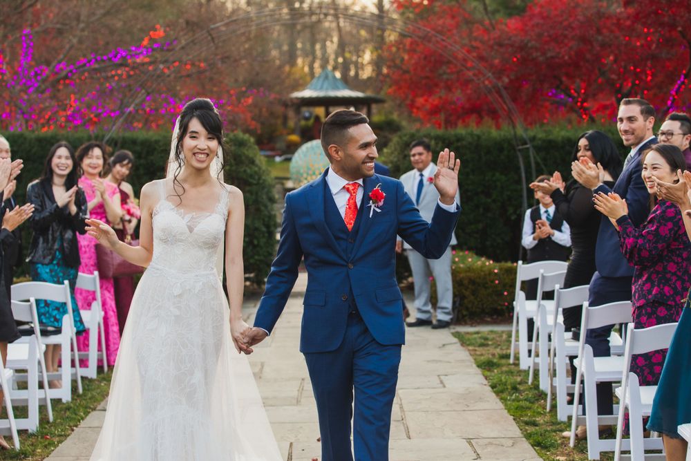 Newlyweds walk down aisle while guests cheer during outdoor fall wedding ceremony.