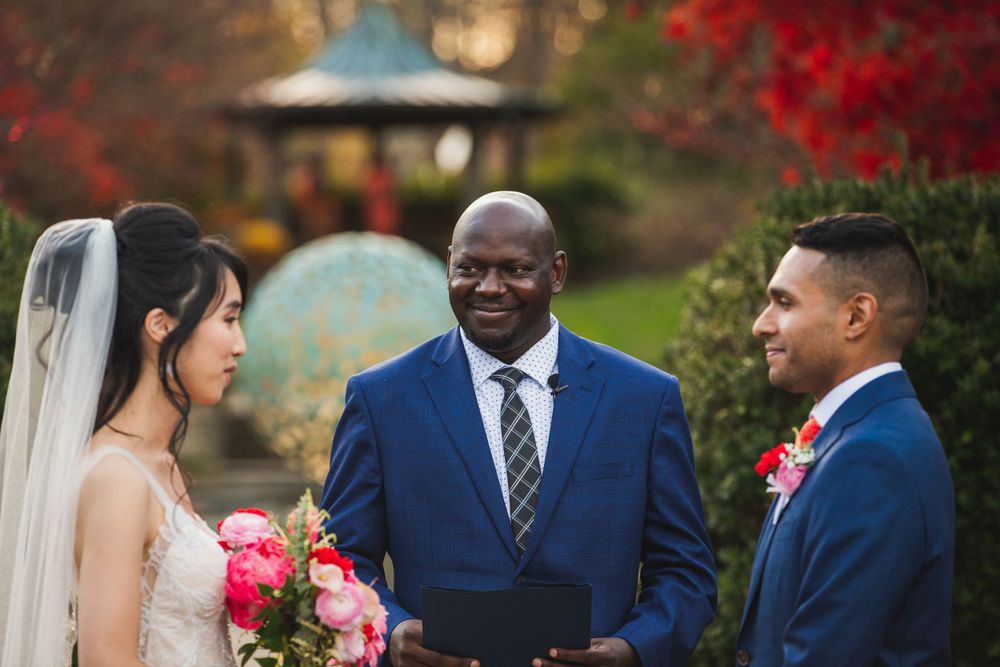 Officiant smiling at bride and groom with wedding gazebo at Brookside Gardens as backdrop.