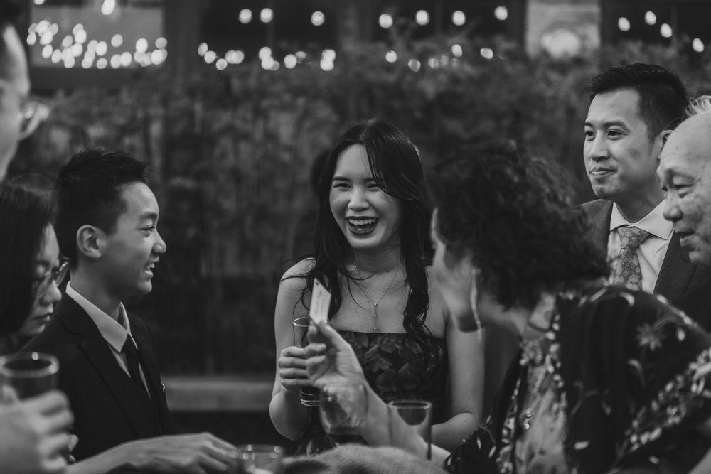 Black and white photo of wedding guests laughing and socializing at evening reception.