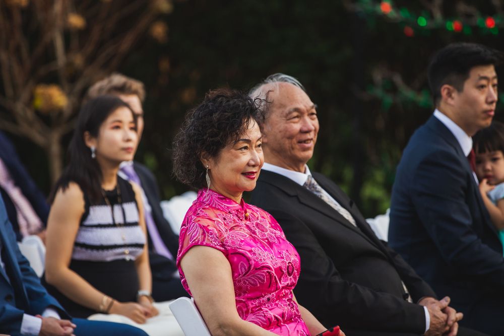 Wedding guests seated outdoors wearing formal attire including traditional pink qipao dress.
