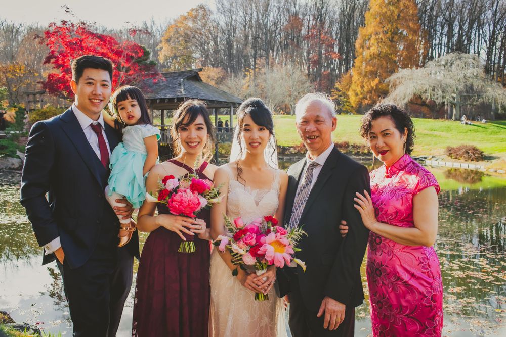 Wedding group photo with family members in formal attire by autumn pond landscape.