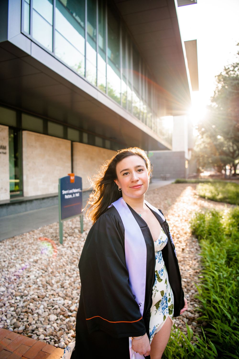 Sunset graduation photo session outside a modern university building with glass walls.