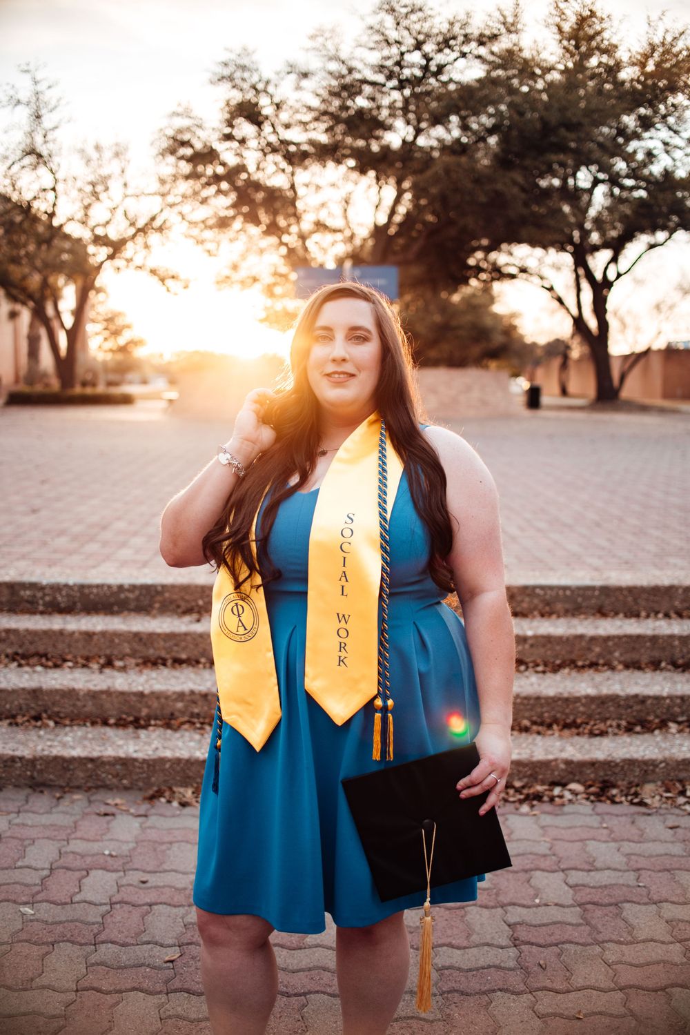 Graduation photos at sunset featuring blue graduation gown and gold stole decorations.