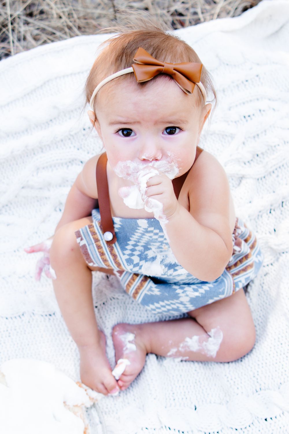 Baby wearing a blue and white striped outfit lies on a white blanket.