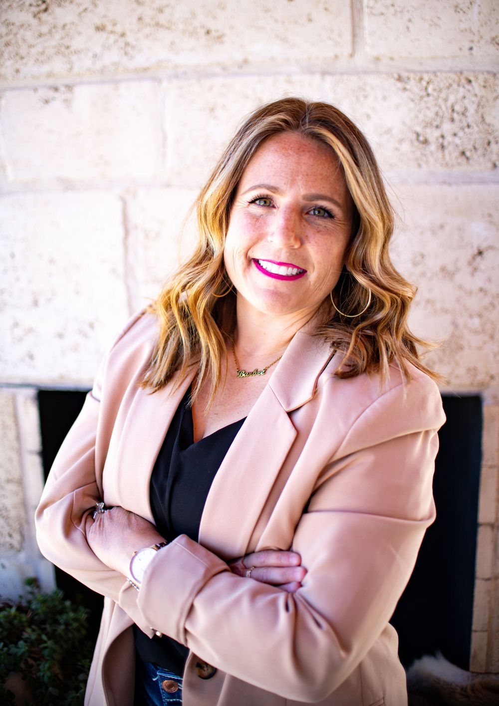 Professional woman in pink blazer smiling against stone wall in outdoor portrait series.