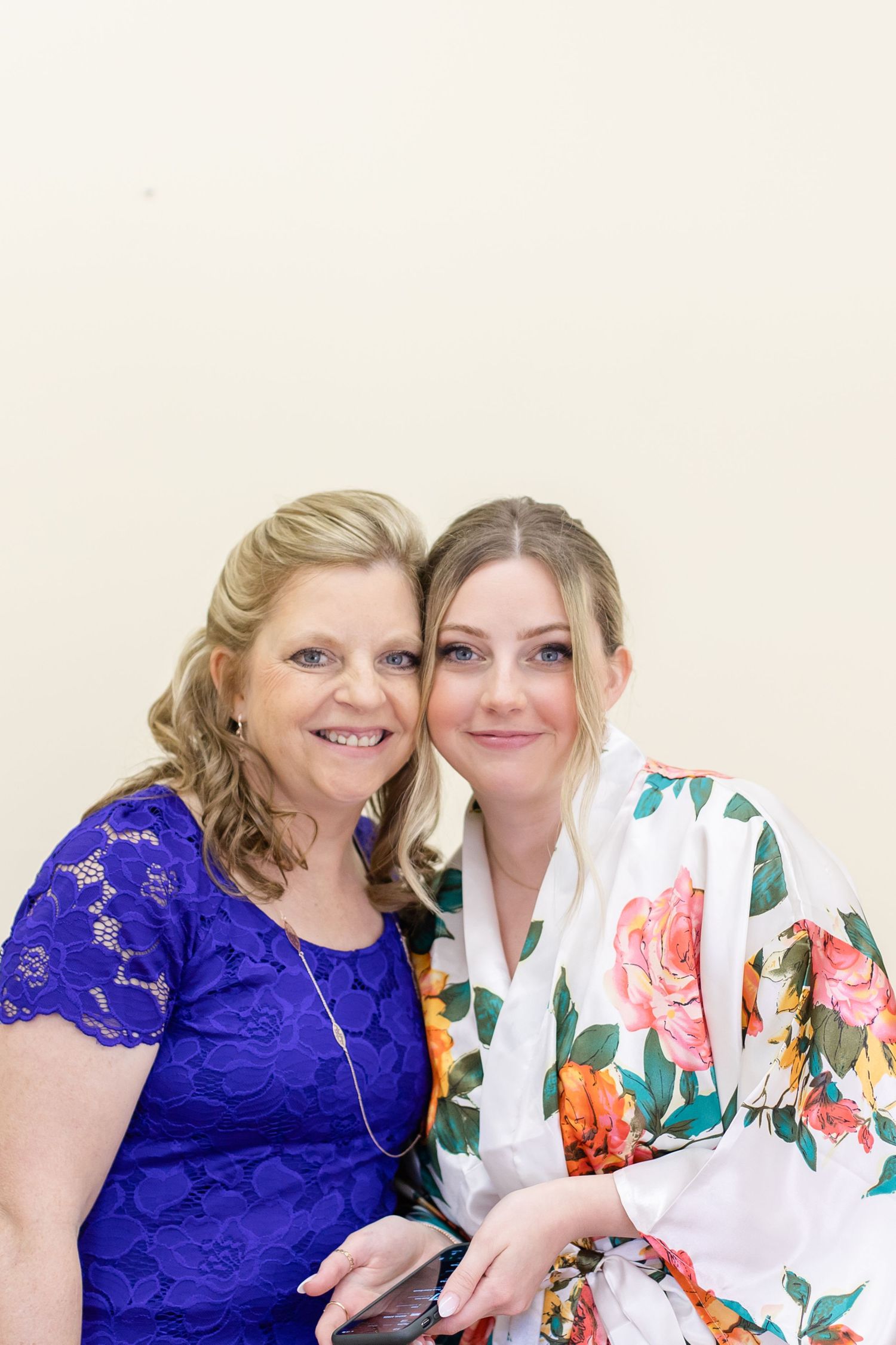 Two women wearing a royal blue lace dress and floral print dress share a joyful moment together.