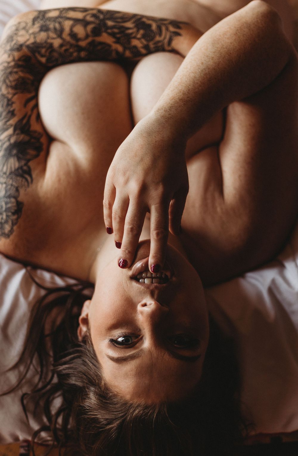 Close-up artistic boudoir photo showing intricate tattoo details on skin in warm lighting.