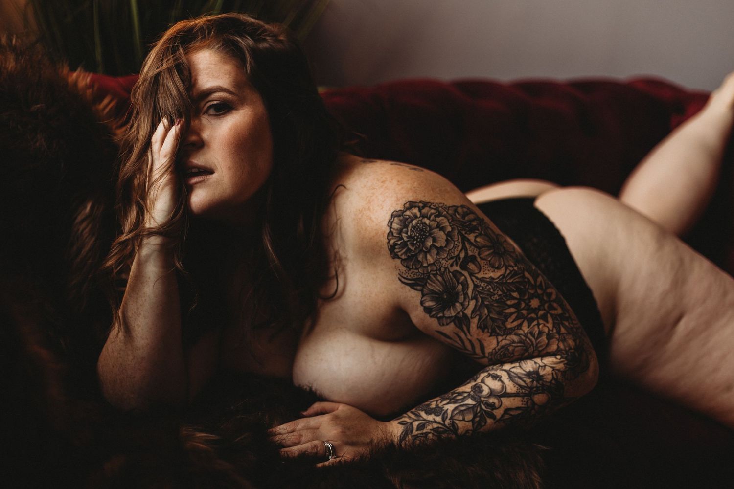 A boudoir photo features a tattooed arm and flowing dark hair in moody, dramatic lighting.