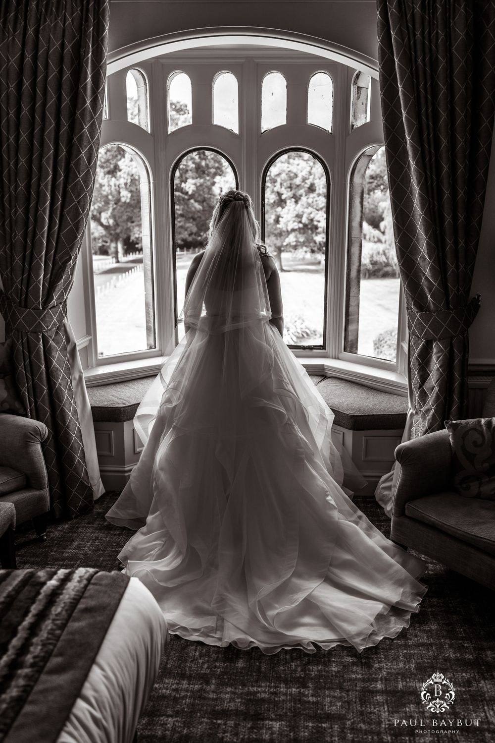 Dramatic black and white photo of a bride silhouetted in an ornate bay window.