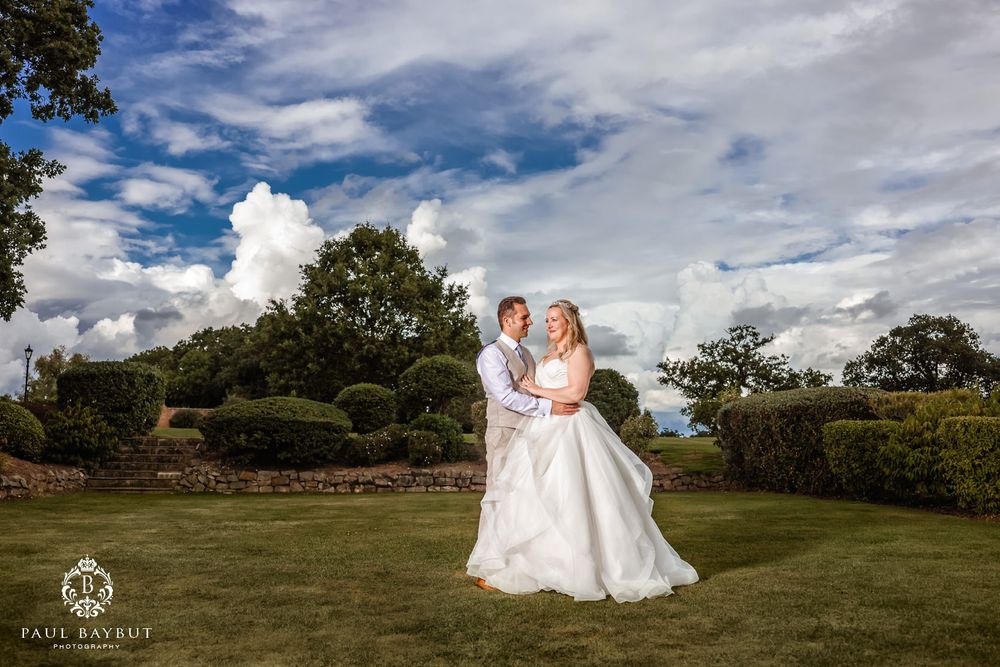 Newlyweds pose together on a lush green lawn under dramatic clouds on their wedding day.