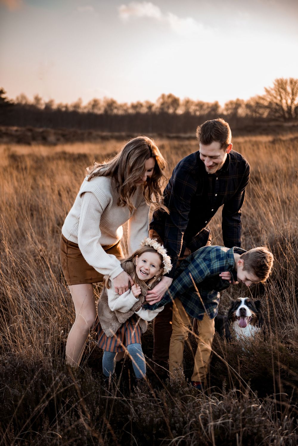 Spontane gezinsfoto van vier met de hond bij een mooie avondzon en warme herfstkleuren