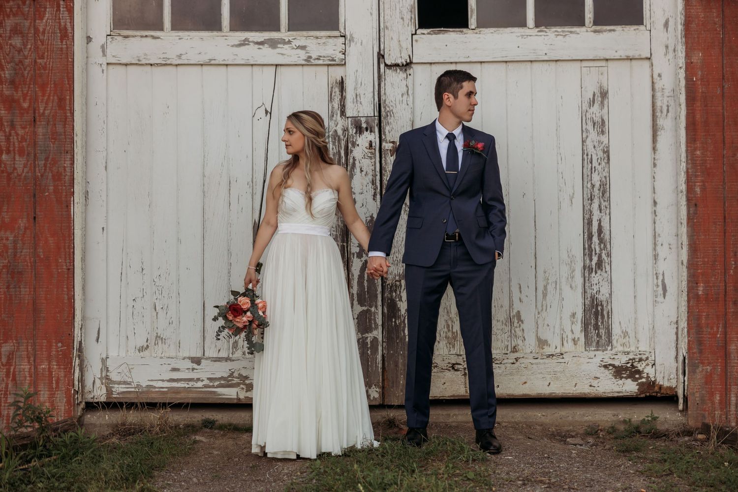 Elegant wedding couple posing against rustic white barn doors.