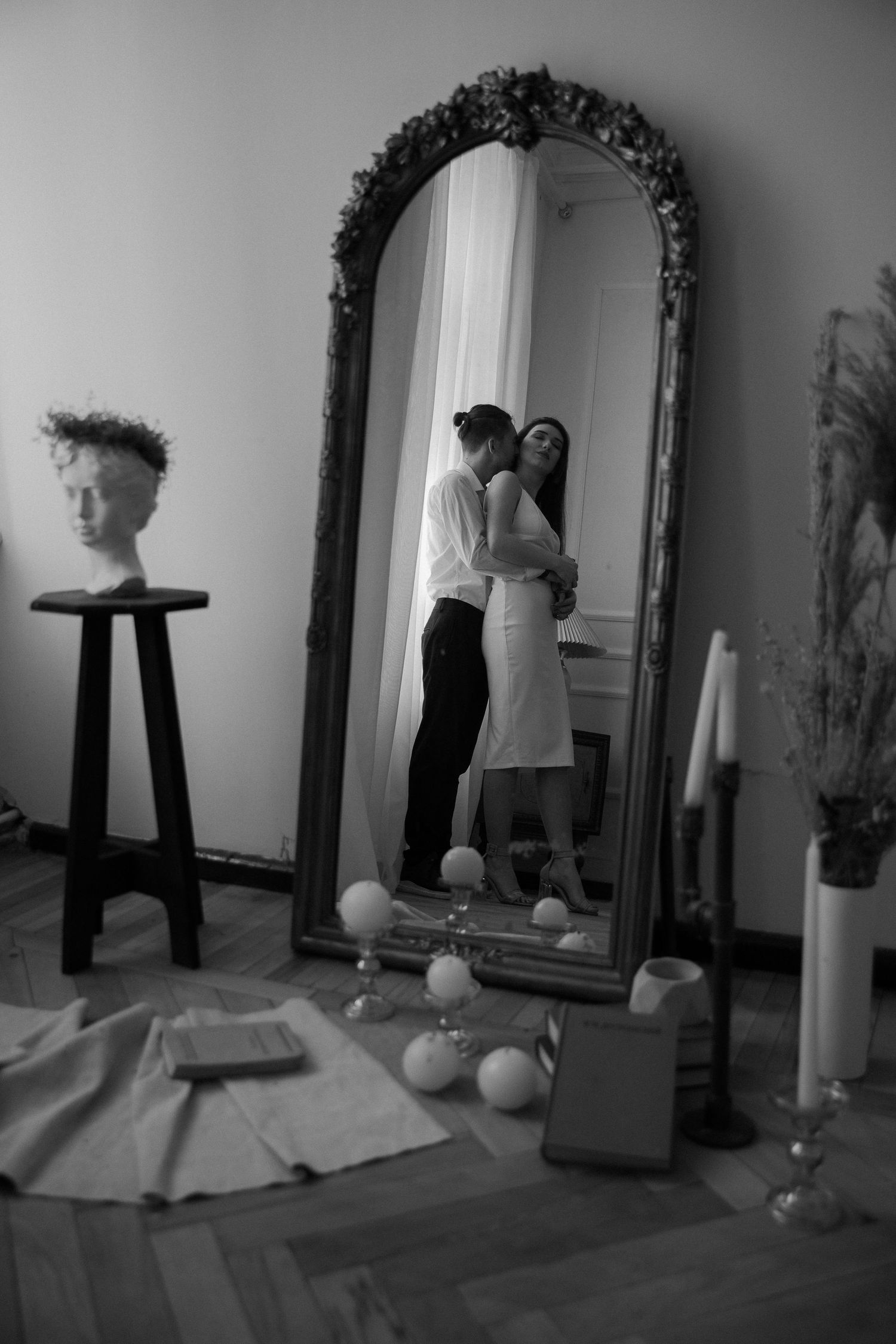 Black and white reflection of couple in ornate mirror with romantic decor.