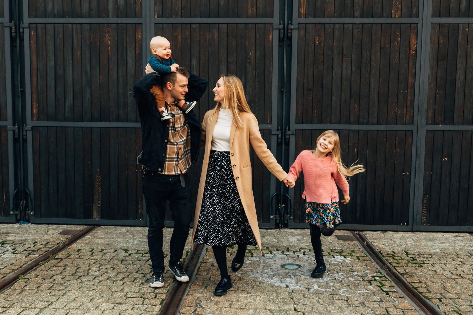 Joyful family with baby and young girl walking and laughing near wooden barn doors.