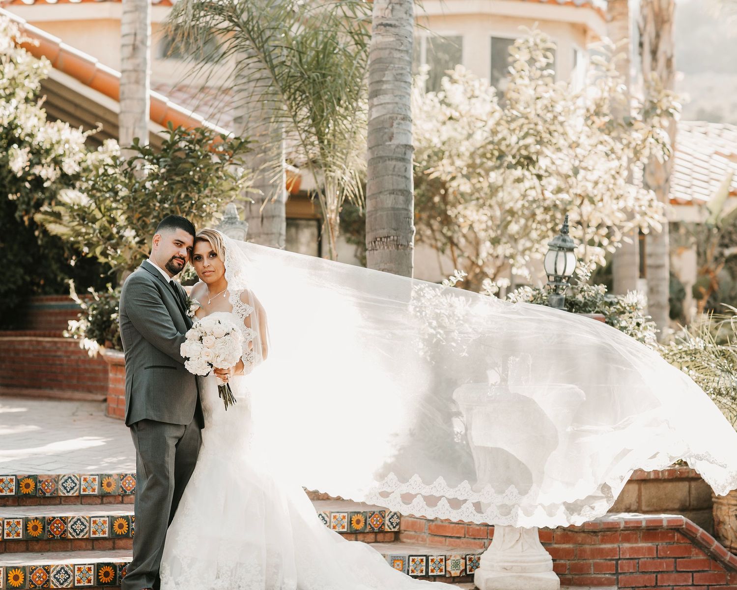 Wedding couple poses for dramatic photos with flowing veil against Spanish architecture.