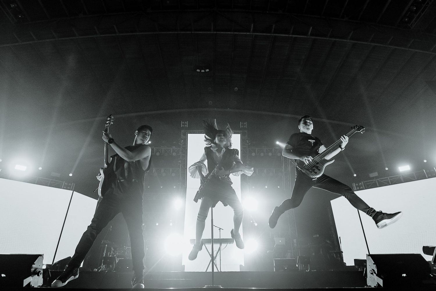 Silhouetted performers jumping in synchronized motion on stage with bright backlighting.