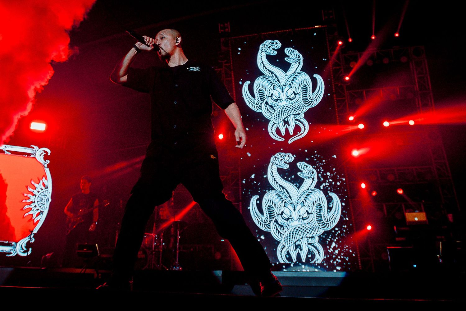Concert performance with glowing blue serpent emblems against red stage lighting.