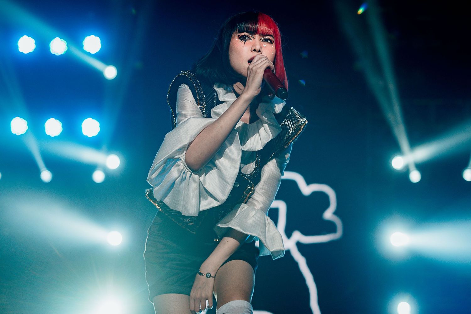 Concert performer with red hair singing on stage with blue stage lights in background.