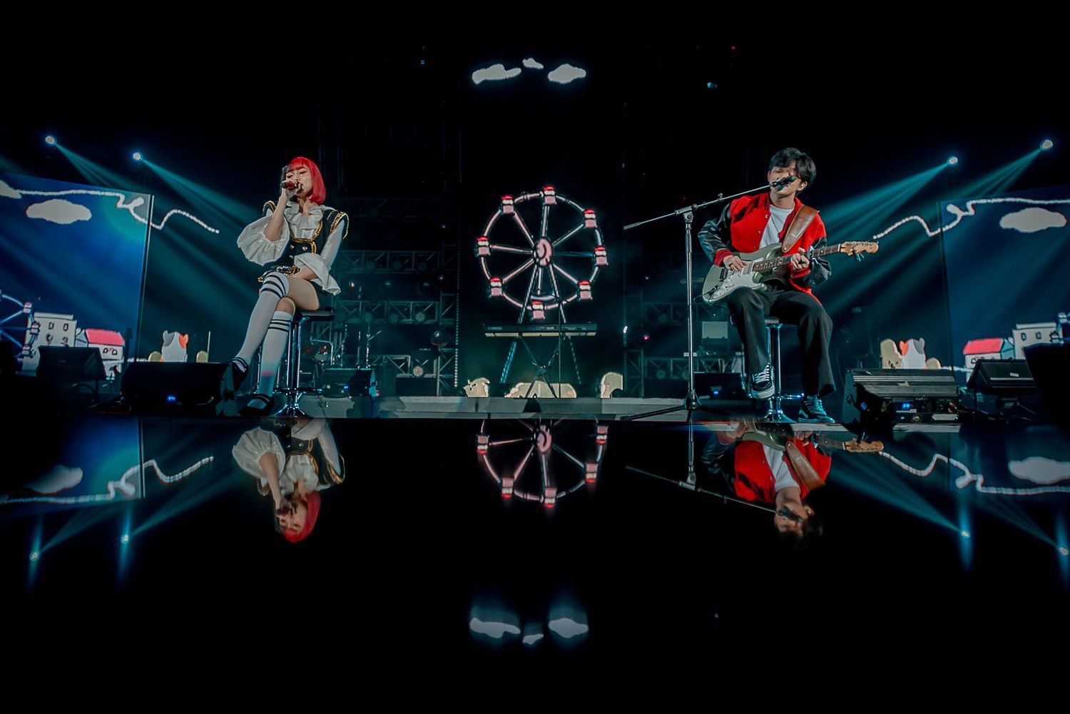 Mirrored stage setup with performers and a ferris wheel prop creating symmetrical reflection.