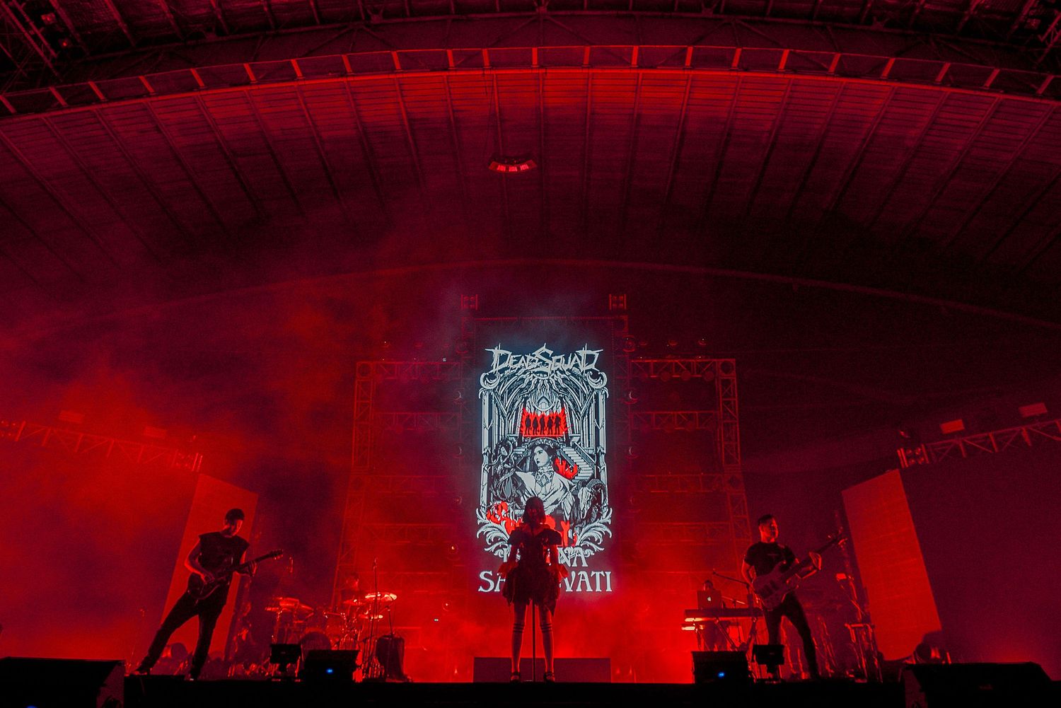 Concert stage bathed in red lighting with neon sign and atmospheric smoke effects.