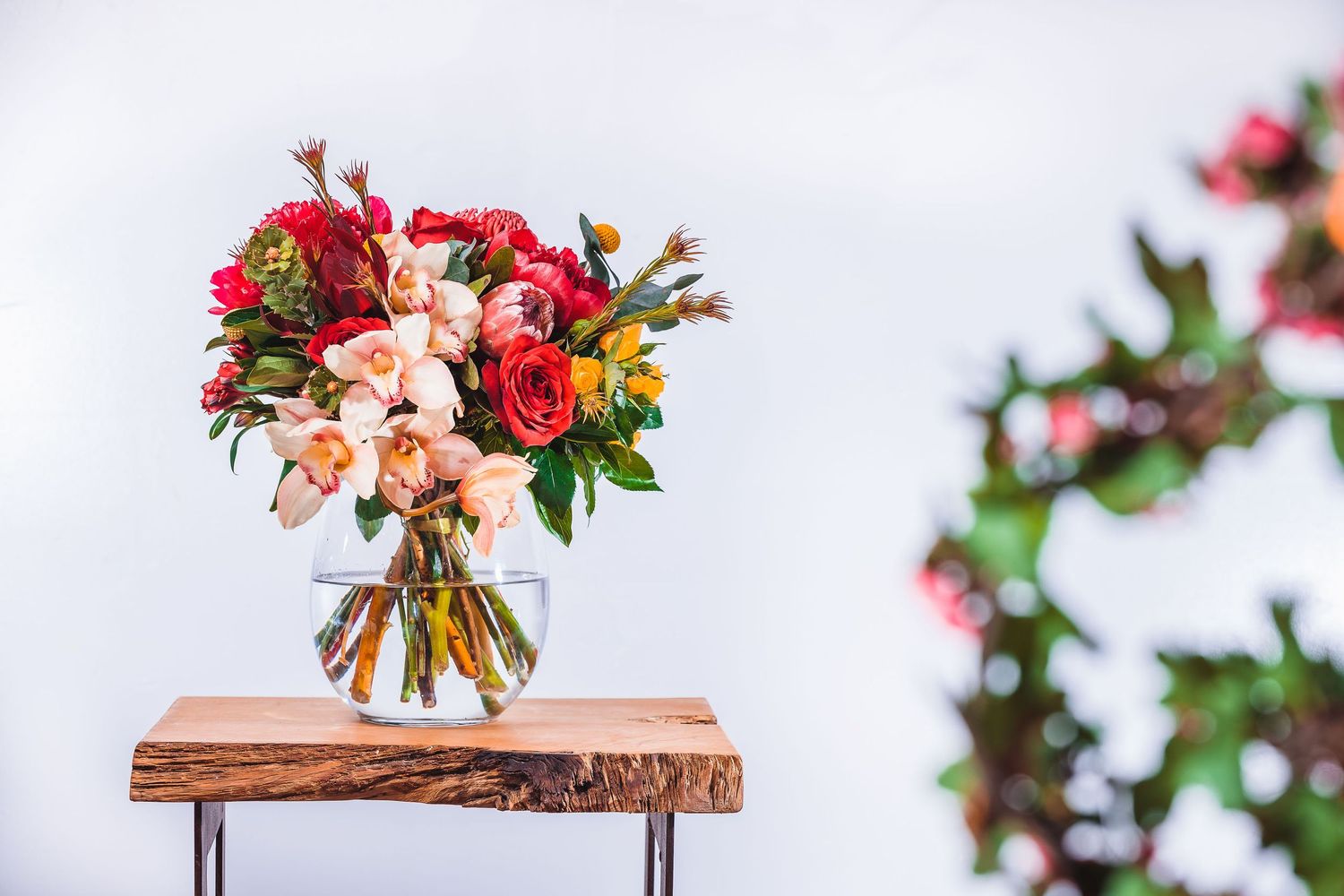 Colorful bouquet of roses and mixed flowers in glass vase on live edge wooden shelf.